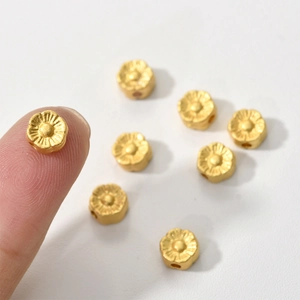 Macro view of gold flower-shaped loose beads for DIY jewelry held on a fingertip