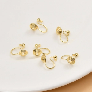 Macro shot of six 14k gold plated spiral clip-on earring converters on white ceramic