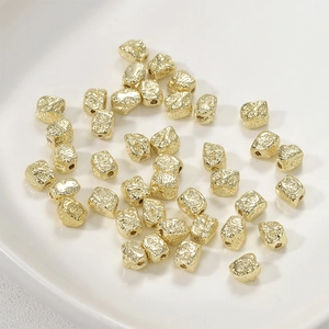 Textured gold irregular metal beads for DIY jewelry making in a white ceramic dish