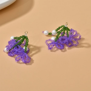 Orecchini a fiore fatti a mano con perle viola e dettagli verdi su sfondo neutro