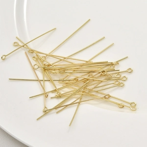 Polished 14k gold eye pins for jewelry making displayed on a white ceramic dish