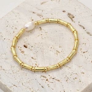 Gold bamboo tube beads and pearl bracelet on a light stone textured background