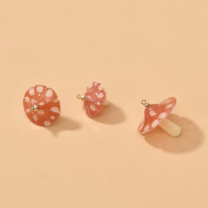 Macro detail of red acrylic mushroom charms with white dots and gold loops for DIY jewelry