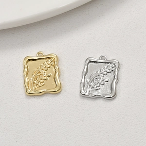 Macro detail of rectangle 14k gold and silver pendants with embossed botanical grain pattern