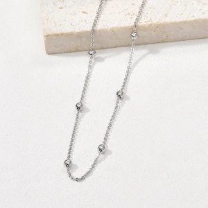 Polished silver beaded necklace chain displayed on a minimalist stone block for jewelry DIY