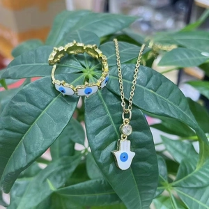 Parure de bijoux Hamsa dorée avec breloques œil bleu sur fond de feuilles vertes