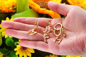 Makroaufnahme goldener Huggie-Ohrringe mit Zirkonia-Buchstaben auf Sonnenblumen-Hintergrund