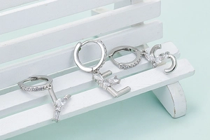 Detailansicht silberner Buchstaben-Ohrringe mit Zirkonia auf einem kleinen weißen Stuhl