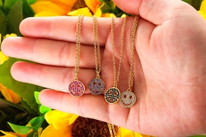Detail of four colorful zircon smiley face necklaces held against a sunflower backdrop