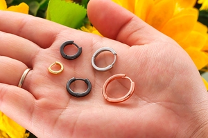 Hand hält minimalistische Edelstahl-Ohrringe in verschiedenen Größen und Farben