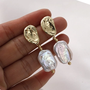 Handheld view of baroque pearl drop earrings with hammered gold metal accents