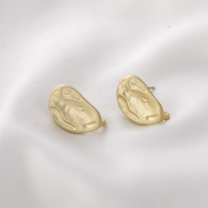 Macro shot of matte gold irregular lava textured alloy stud earrings on white silk fabric