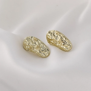 Close-up of golden teardrop earrings with hammered texture and floral engraving on silk