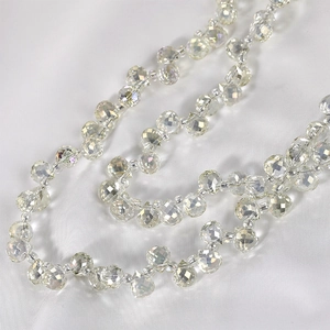 Macro detail of faceted iridescent crystal teardrop beads on white silk fabric