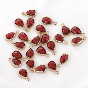 Macro view of teardrop red faceted glass charms with gold metal edges and hanging loops