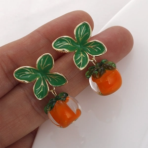 Detail of handmade persimmon glass earrings with green leaves and orange pendants