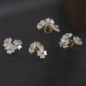 Close-up of mother of pearl four-leaf clover charms with gold beads on black background