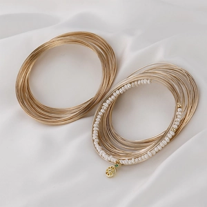 Dettaglio di bracciali a molla placcati oro 14k con perle bianche e ciondolo rotondo