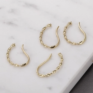 Detailed view of four twisted gold-plated ear cuffs on a white marble background