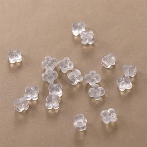 Transparent flower-shaped silicone earring backs in bulk on a golden brushed surface