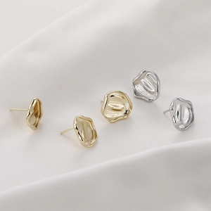 Irregular textured gold and silver metal earrings on white fabric background