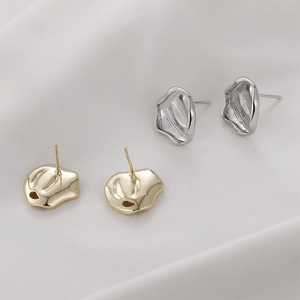 Irregular textured gold and silver metal earrings with lava petal design on white cloth