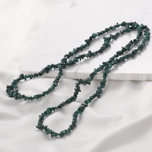Macro shot of natural green malachite irregular chip beads on white marble and silk