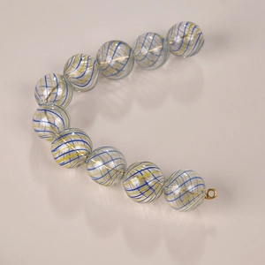 Detailed macro of hollow glass bead with blue and yellow lines and gold metal clasp