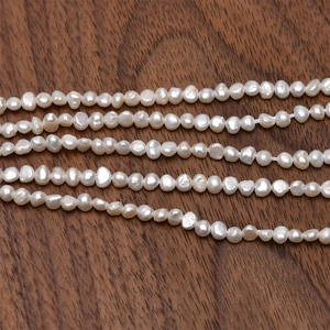Dettaglio di perle naturali barocche bianche da 3-4 mm su sfondo in legno scuro