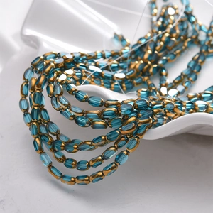 Macro shot of faceted lake blue oval glass beads with gold trim in a white ceramic dish