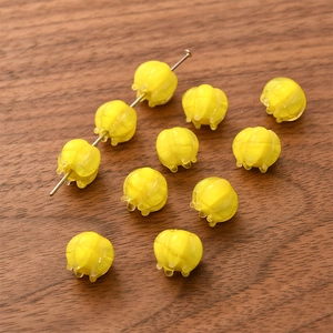 Macro shot of 10 yellow pumpkin-shaped glass beads and metal pin on wood surface