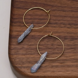 Detailed macro view of gold hoop earrings with irregular light blue crystal agate pendants