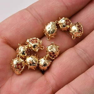 Close-up of small 14K gold plated strawberry charms with red zircon stones in hand