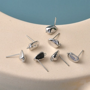 Close-up of silver pebble-shaped DIY earring studs with loops on ceramic display