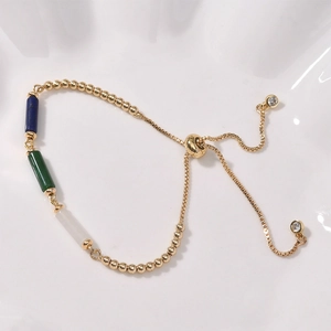 Adjustable gold chain bracelet with colorful cylinder beads on a white ceramic plate