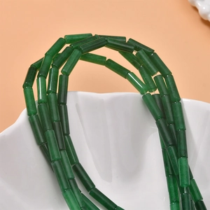 Close-up of green cylindrical semi-precious stone beads in a decorative white ceramic bowl