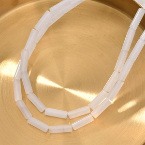 Macro detail of white cylindrical quartz beads on a textured golden tray for DIY jewelry