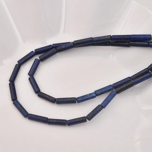 Macro detail of cylindrical lapis lazuli beads with natural gold flecks on white tray