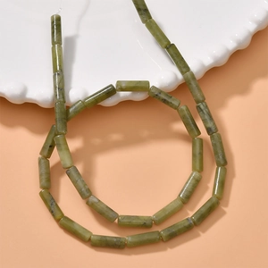 Close-up of natural green stone cylinder beads for DIY jewelry making on white ceramic plate