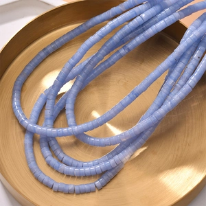 Flat round blue stone spacer beads with white marble texture on a gold tray