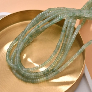 Macro detail of translucent light green natural stone cylinder beads in a golden tray