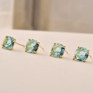 Detailed view of square blue crystal stud earrings with gold four-prong setting