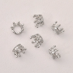 Close-up of six crown-shaped zircon charms for DIY jewelry making in polished silver finish