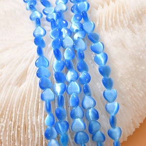 Macro shot of 8mm blue heart cat eye beads arranged on white coral for DIY jewelry