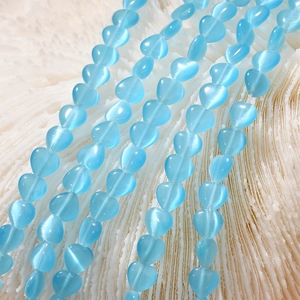 Macro shot of 8mm sky blue heart cat-eye stone beads on white coral background