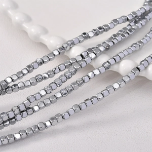 Macro shot of 3x3mm faceted square hematite loose beads on a white textured plate