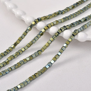 Macro detail of 3mm square hematite beads with iridescent metallic green and blue finish