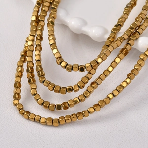Close-up of multilayered necklace with polished gold square beads on a white tray