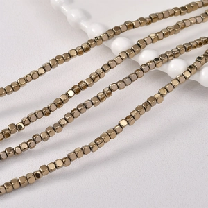 Golden 3x3mm cube hematite beads on a ceramic tray for DIY jewelry making and crafts