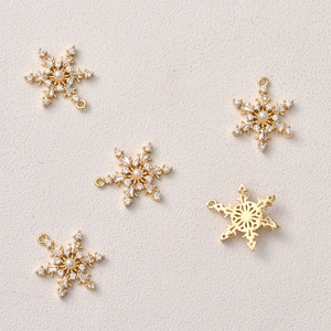 Detailed close-up of 14k gold plated snowflake pendants with zircons and pearls for DIY
